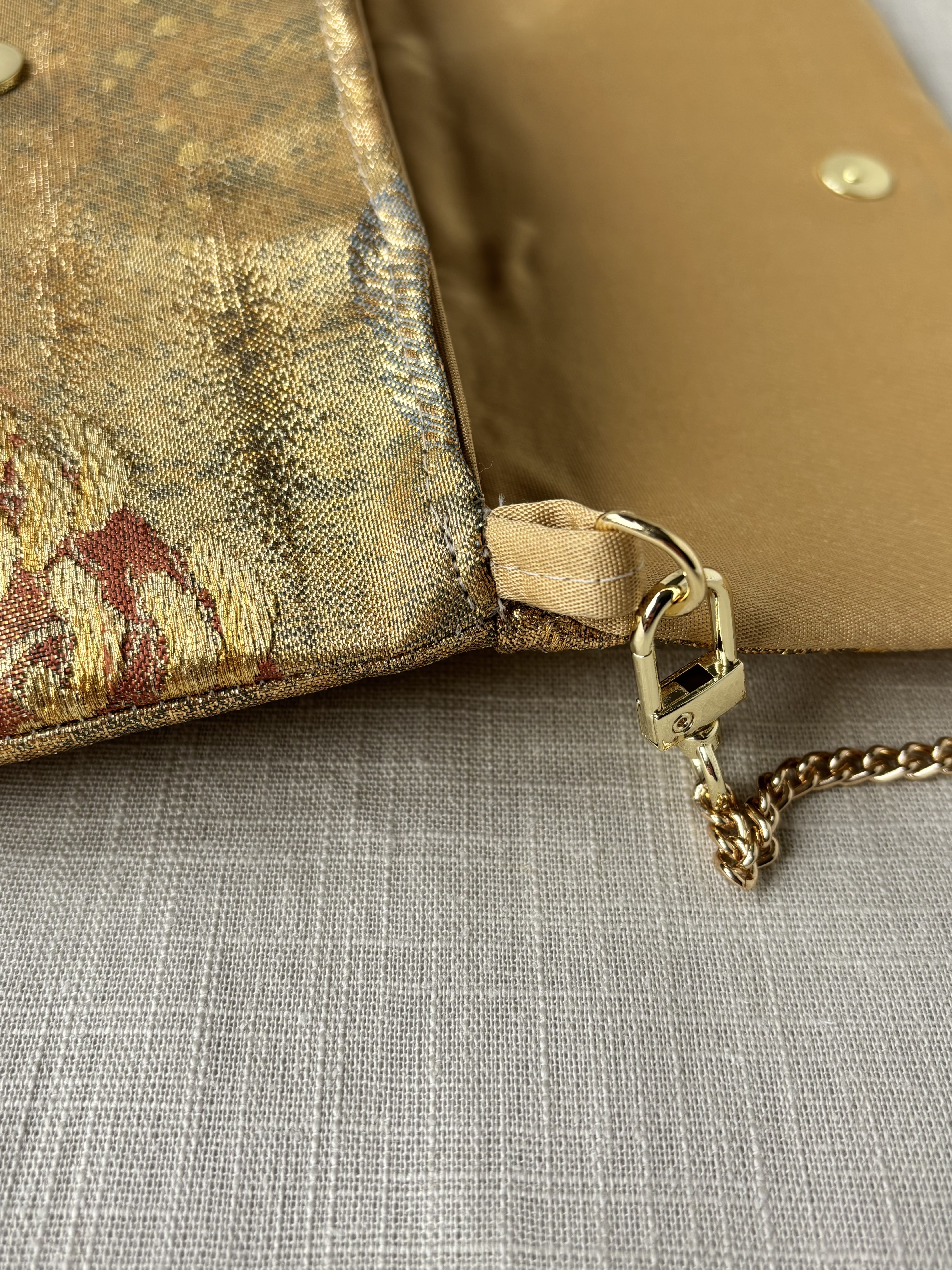 Image of a close-up of the side of the clutch showing the structure of the metal threads of the obi and the polished chain loop with attached gold coloured chain.