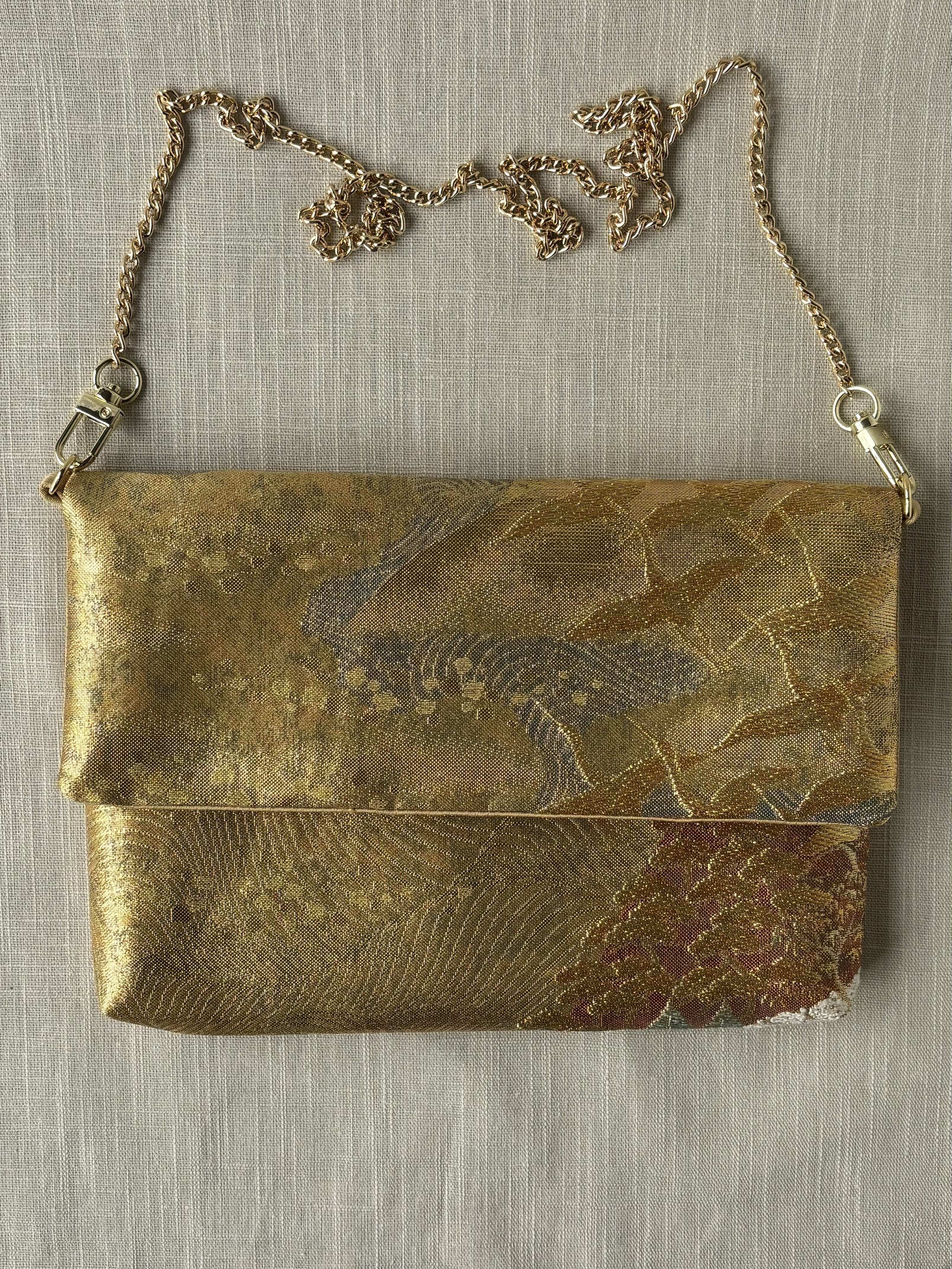 Front view of the clutch with attached chain, showing a group of cranes flying across a backdrop of mountains and rust coloured wood.