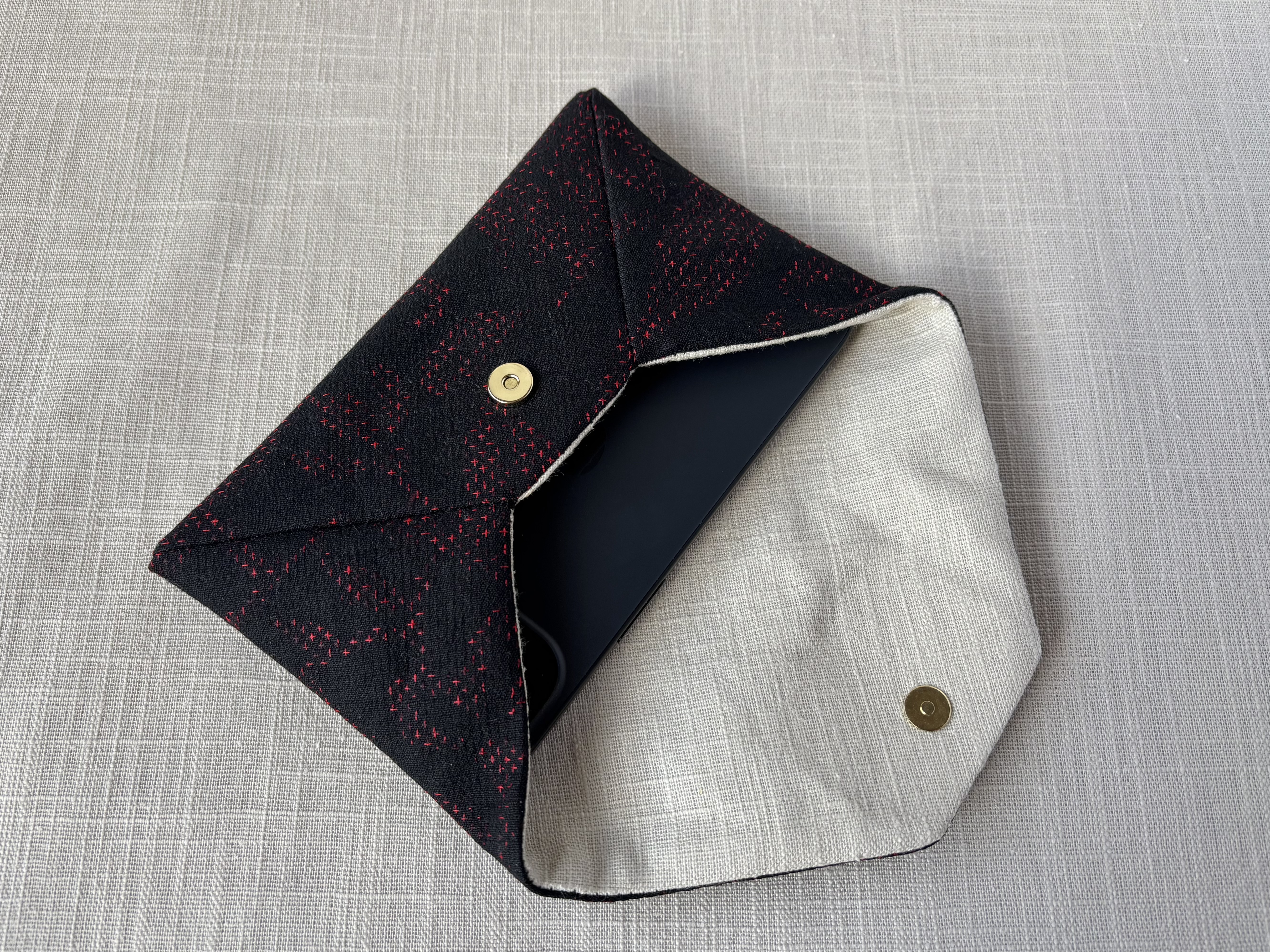 Side view of the sukiya bag showing an iPhone 15 inside on a cream coloured textured linen background.